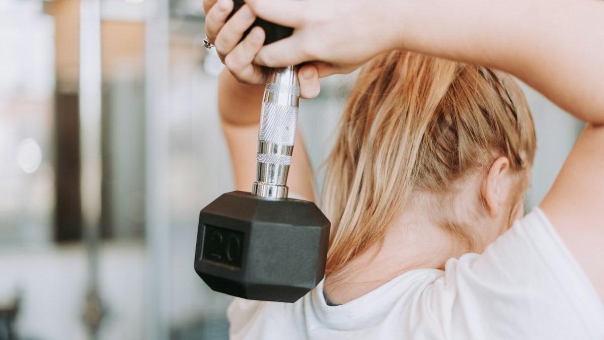 woman holding dumbbell in white crew-neck t-shirt